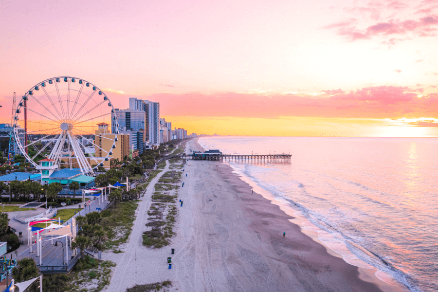 A beachfront aerial view at sunrise of Myrtle Beach, with a Ferris wheel and pier in the background