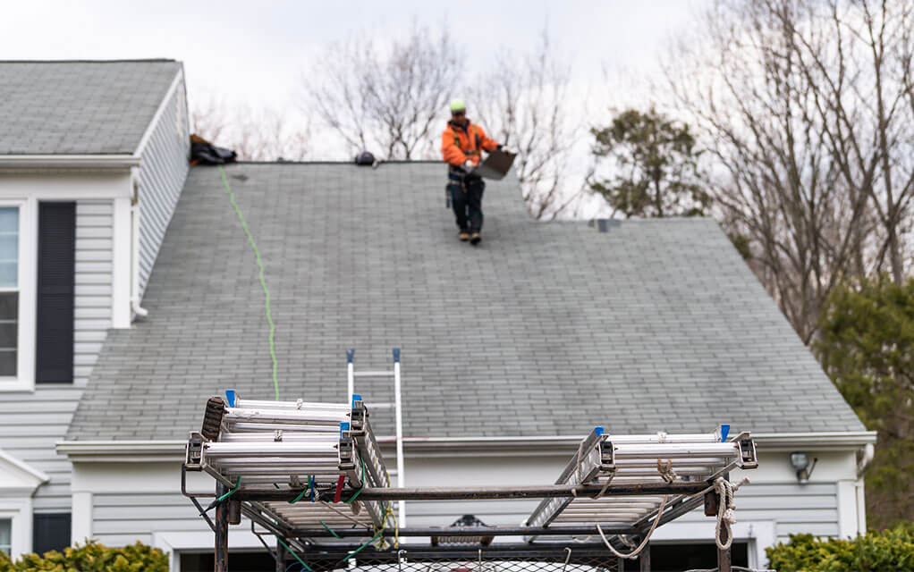 An inspector carries roofing materials down the roof of a residential home on a cold and cloudy day