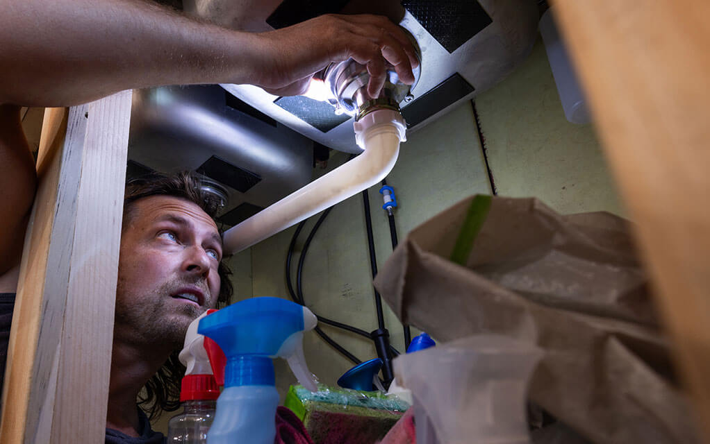 A man works under his sink to provide a fix for an issue in his home