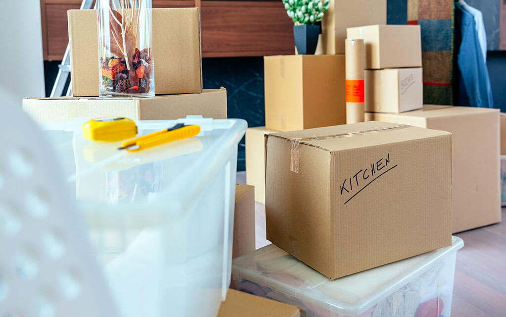 A bunch of boxes lay on the floor of a home with some other packing supplies about on a bright day