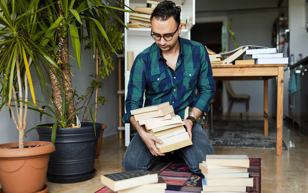 A young man organizes books on the floor of his apartment
