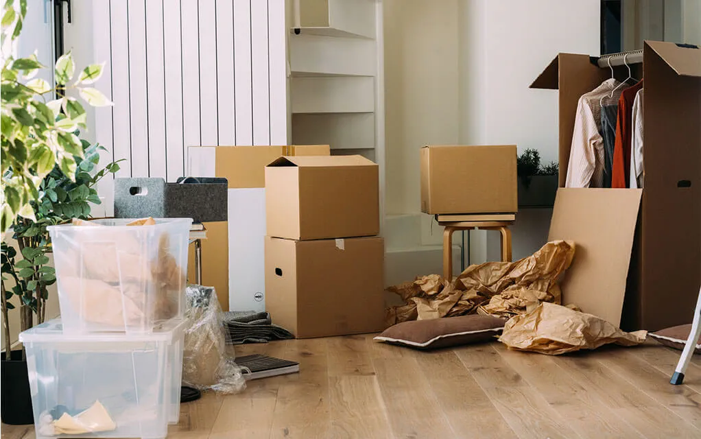 A pile of cardboard boxes and plastic bins lay strewn about a room ready to be taped and packed away for an upcoming move