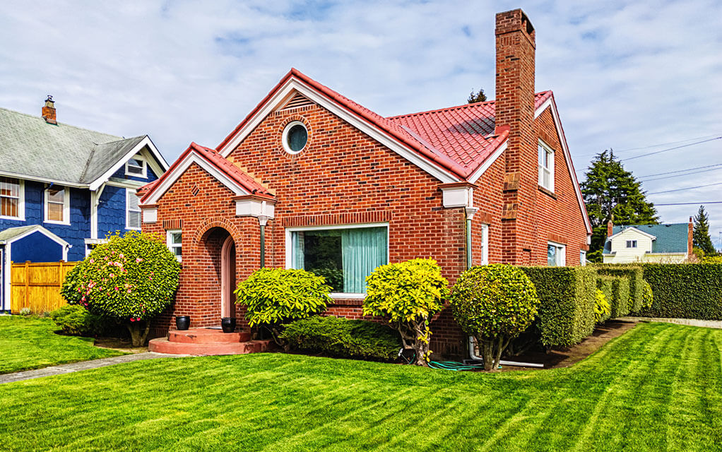 Front view of a small brick home with a manicured front lawn in a quant American suburb on a partly cloudy but bright day