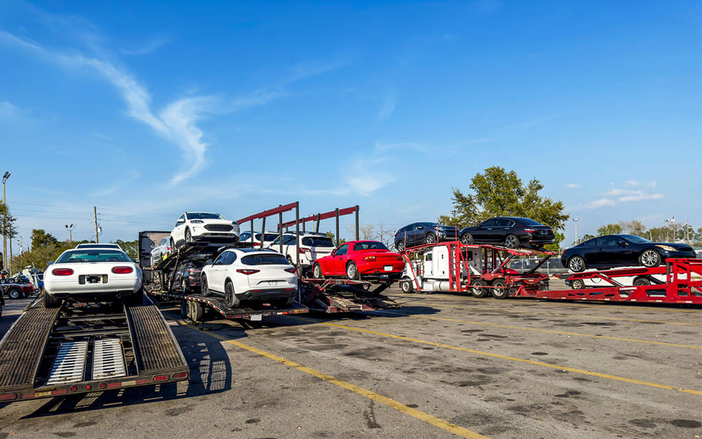 Several long-haul vehicle carrying trucks with vehicles stowed on them sit in a truck rest stop parking lot on a sunny and clear day