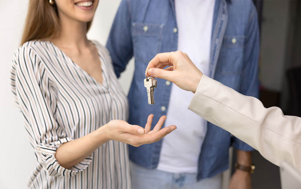 A happy couple smiles as a realtor hands them the keys to their new home
