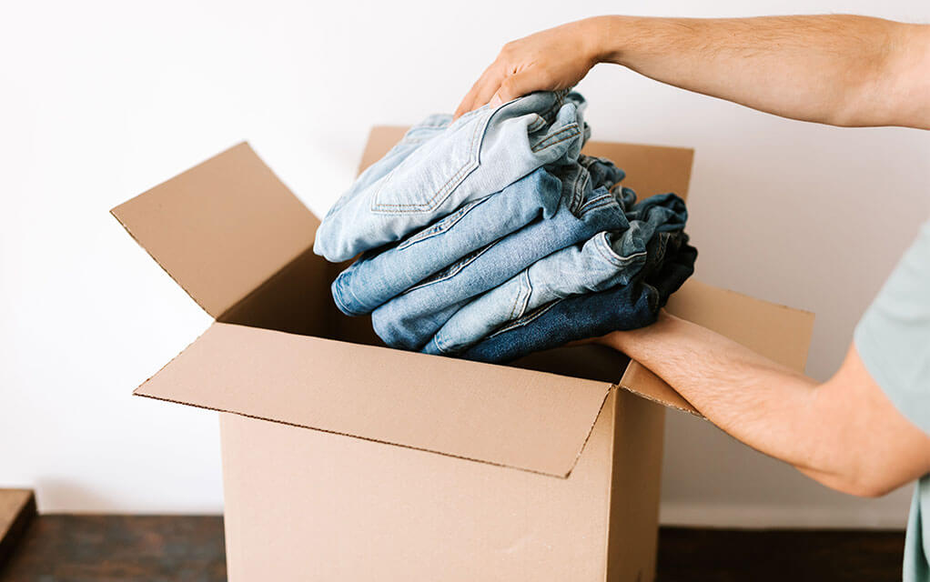 A man packs five pairs of folded jeans into an open moving box