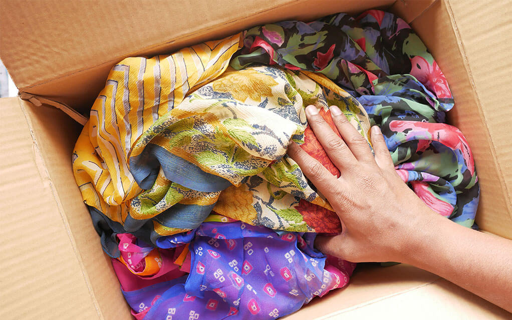 A woman finishes packing an open box full of colorful scarves for a move
