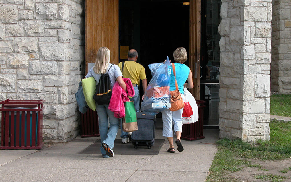 A young college student and her parents carry belongings into front door of a dorm complex as they move her into her new home