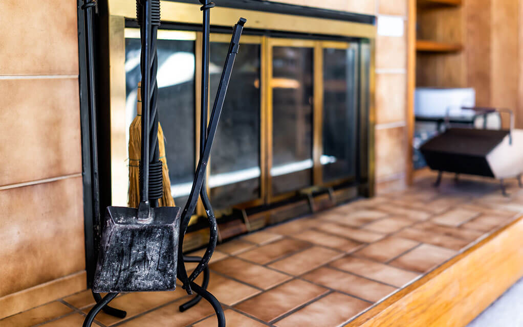 A shot of a modest home fireplace in the background with a scooper and firepoker sitting in the foreground, waiting to be used