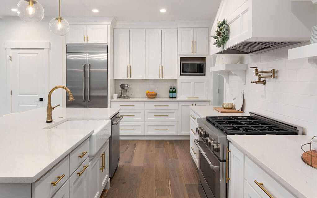 Wide view of a large, upscale home kitchen with a large kitchen island, oven range, fridge, and other regular kitchen appliances and items