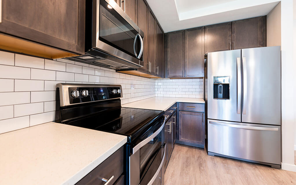 View of a kitchen range, counter, microwave, and stainless steel refrigerator in a modest home