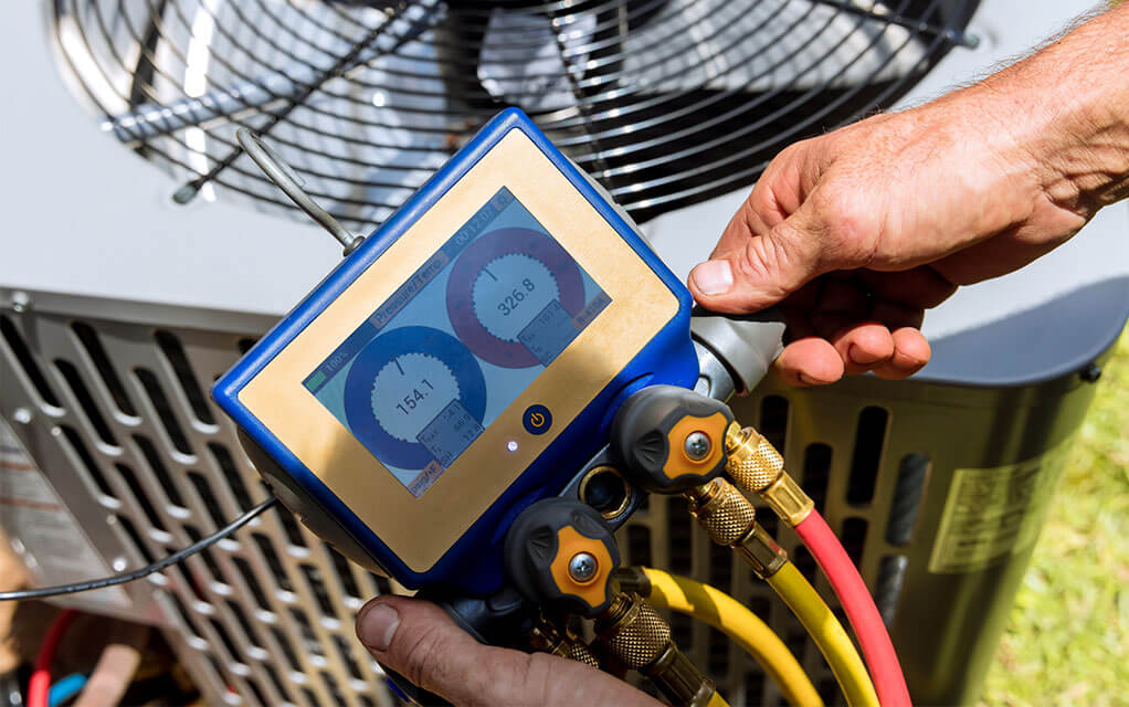 An HVAC technician holds and checks the pressure of an HVAC outdoor unit and system on his HVAC digital pressure gauge