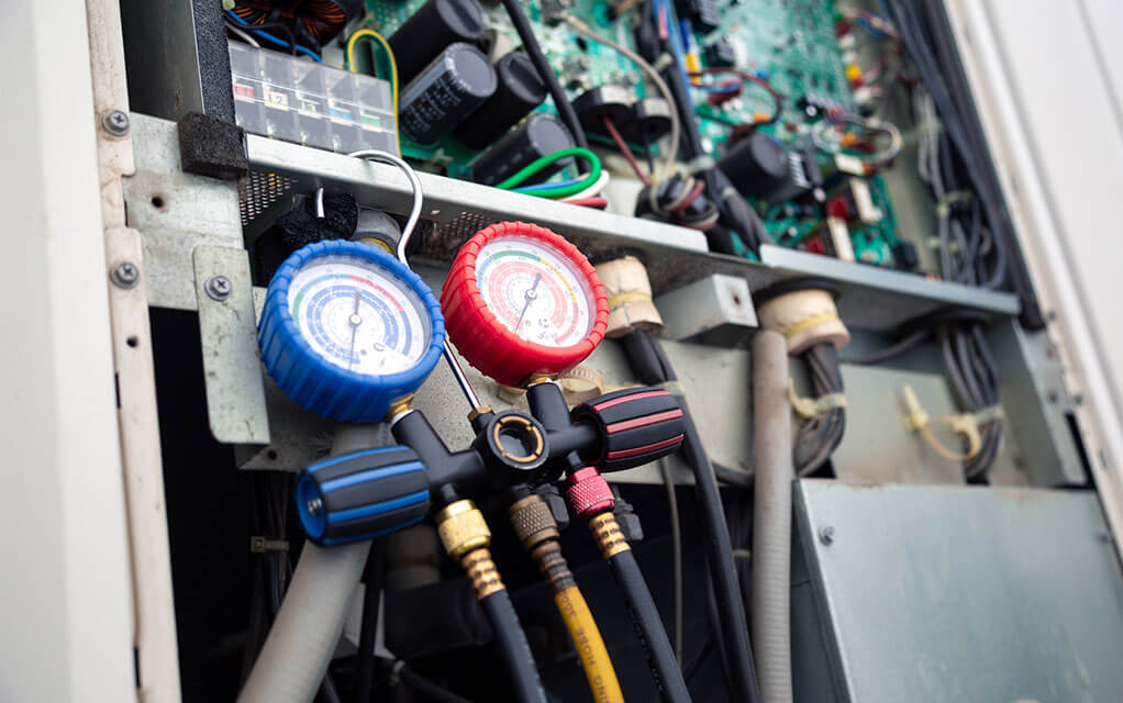 An HVAC pressure gauge is taking a reading from an open outdoor HVAC unit 