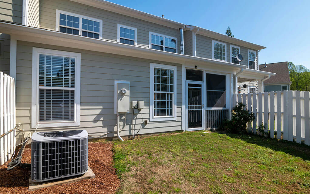 Back view of a townhome with an HVAC unit located right outside the backdoor on a sunny and clear day