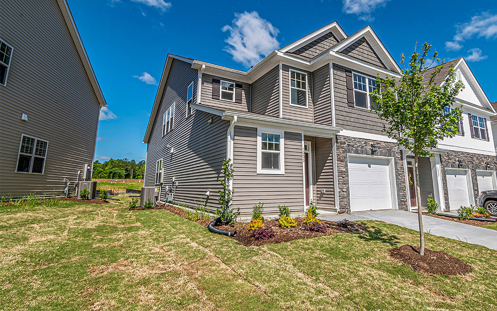 Front view of a suburban townhome and the easement between it and the next block of homes with HVAC outdoor units in view on a bright and sunny day