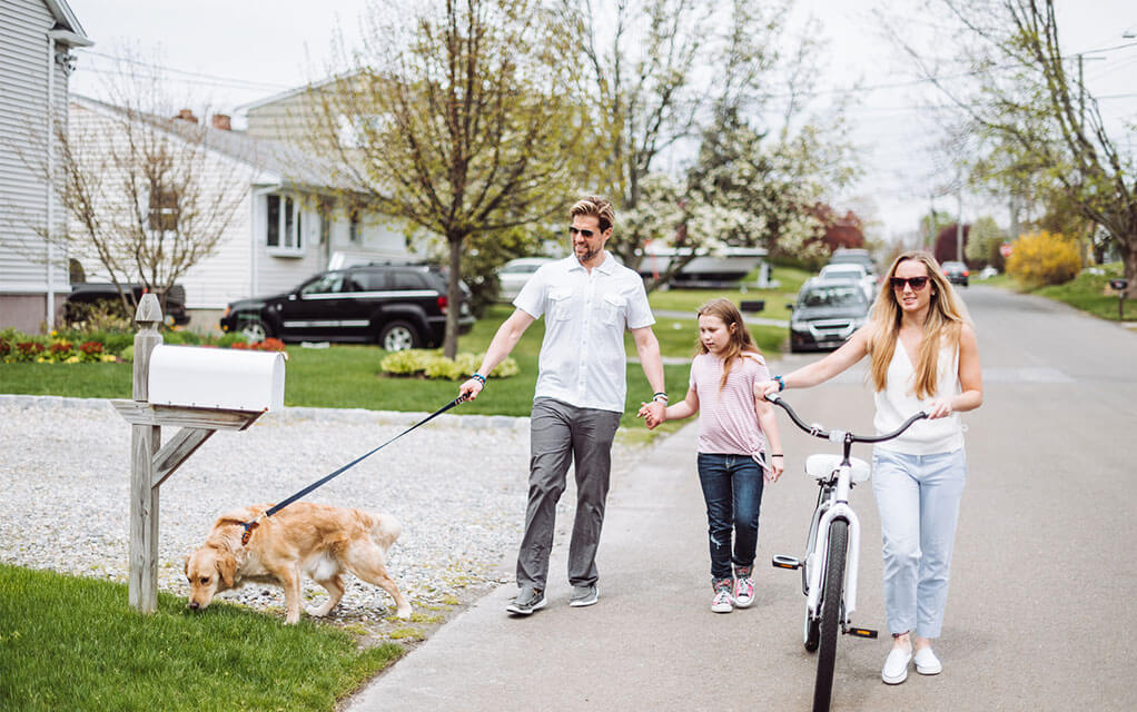A middle aged couple and their daughter and dog all walk down a neighborhood street as a family