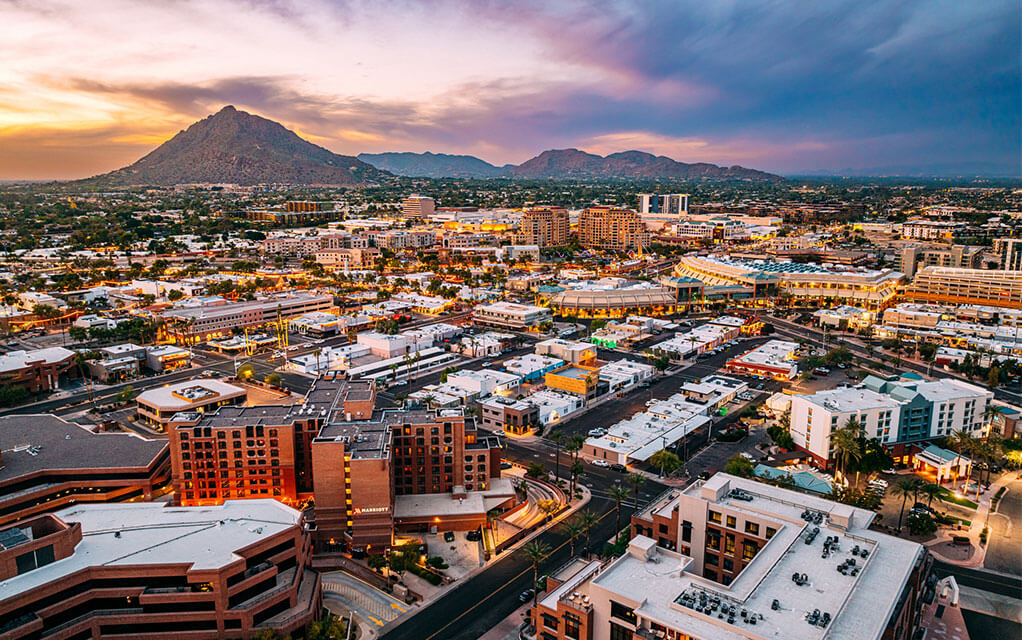 An aerial view of the downtown Scottsdale, AZ cityscape at dusk with mountains in the background