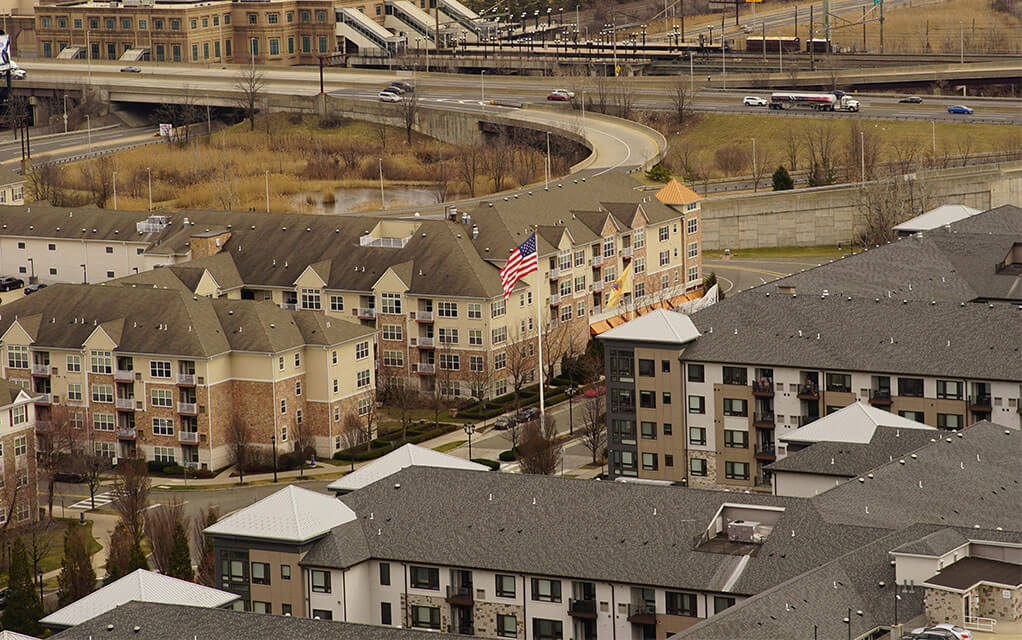 Aerial view of a large apartment complex with multiple large buildings and an American flag on a tall flagpole in the middle of the complex