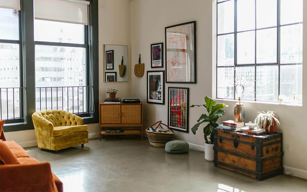A view inside a studio apartment unit with decor and posters on the wall and small yellow felt chair sitting next to a window on a bright and sunny day