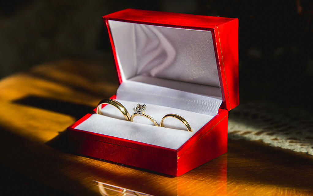 Two gold rings and a diamond ring sit in a red and white ring box on display on a table