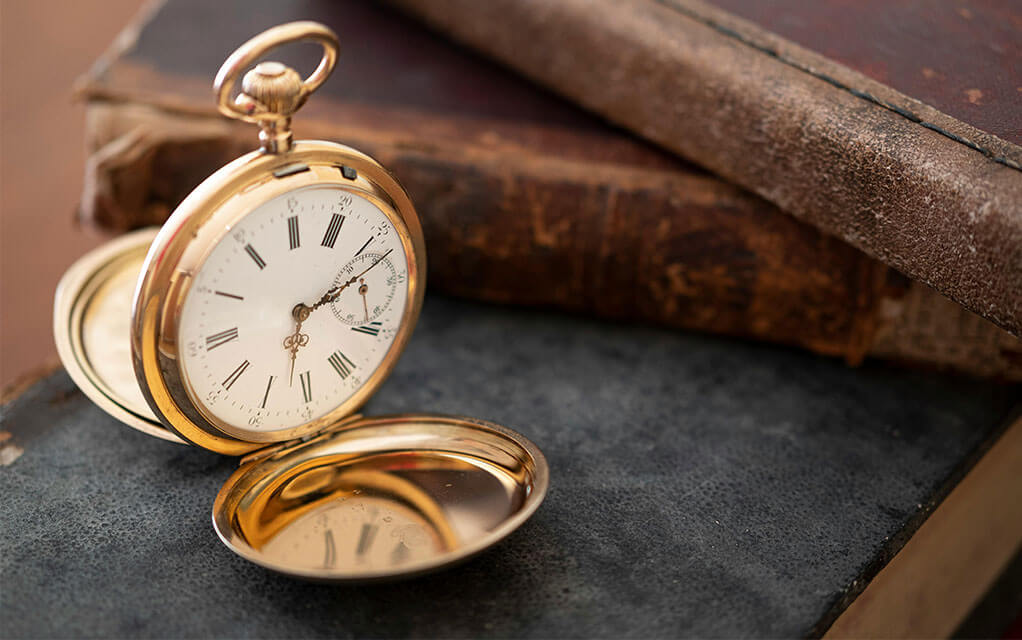 An antique gold pocket watch sits open on top of an old book