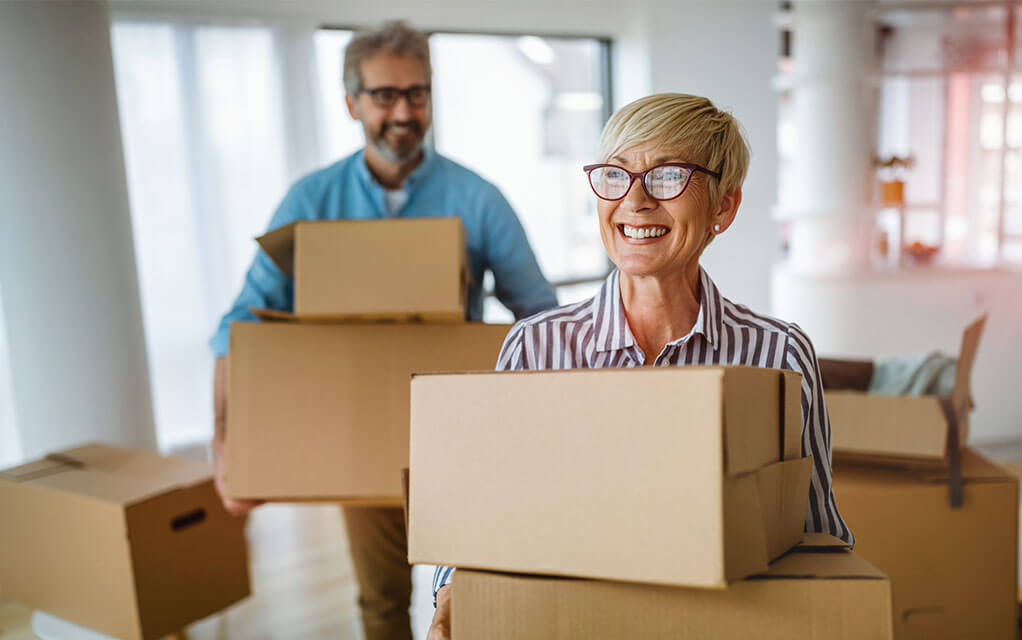 A mature couple smiles as they carry boxes into their new home after a move
