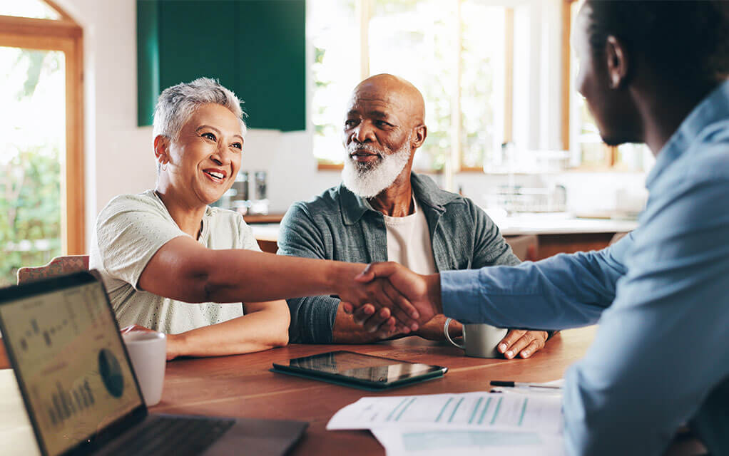 An older couple shakes hands with their financial planner in their home after a meeting