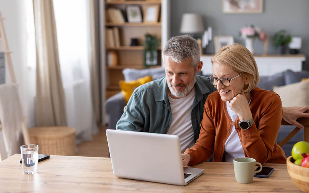 An older couple sits at their table looking at a laptop computer in front of them