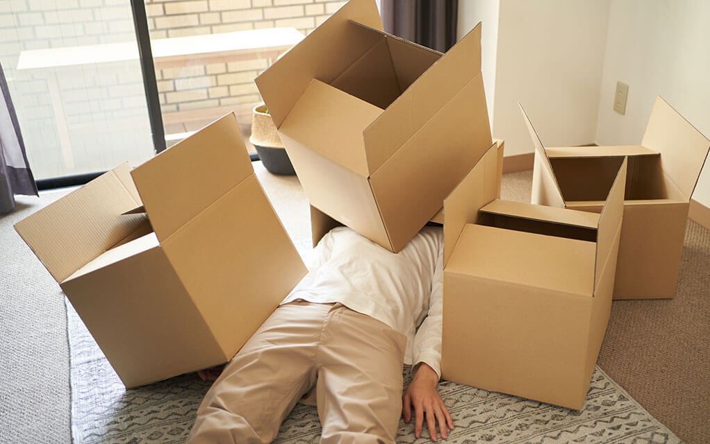 A man lays under a pile of opened moving boxes on a sunny day