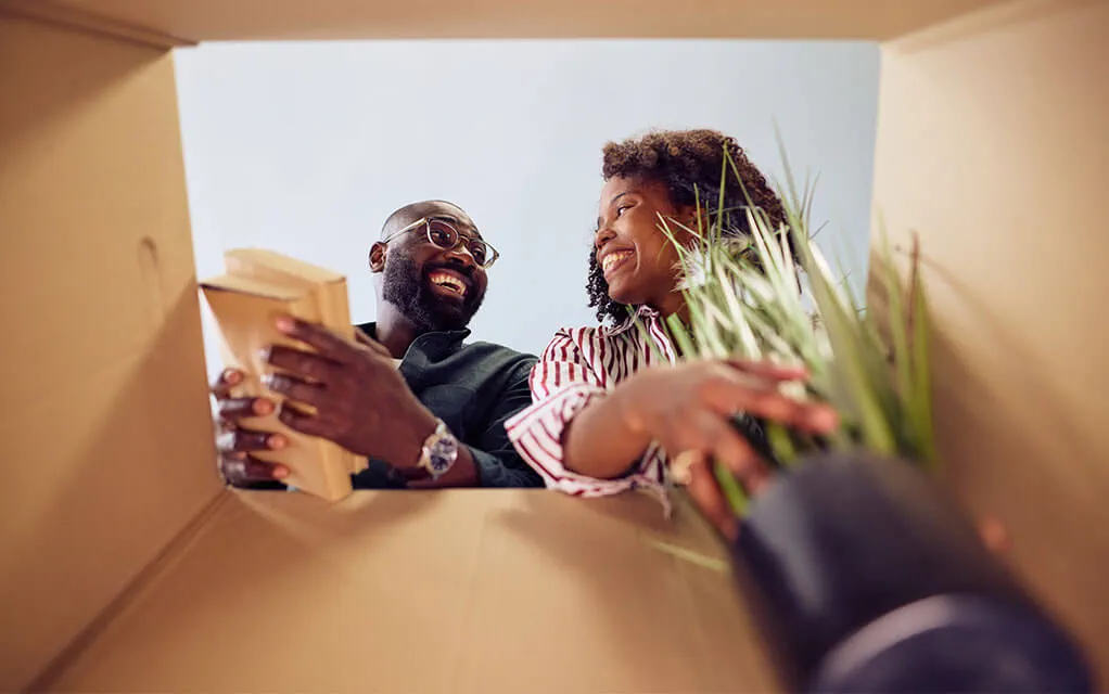 A view from the bottom of a moving box shows a happy couple filling the box with a plant and some books