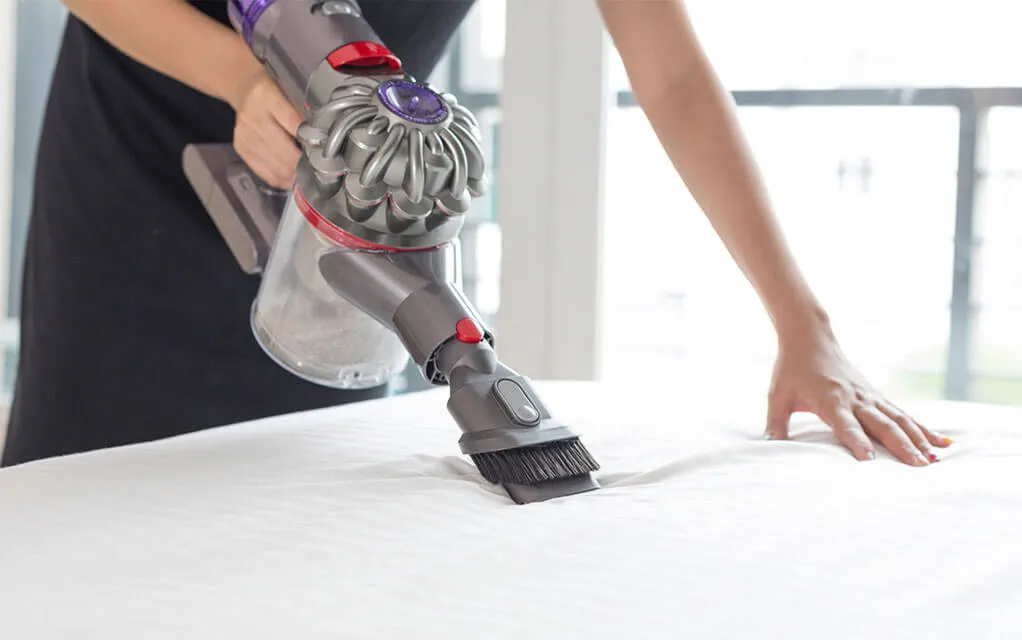 A person uses a wet vac to clean their mattress on a bright day