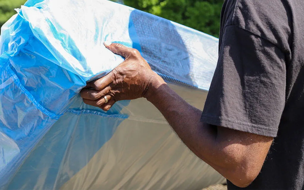 A man holds a mattress that is contained in a mattress bag outside, moving it