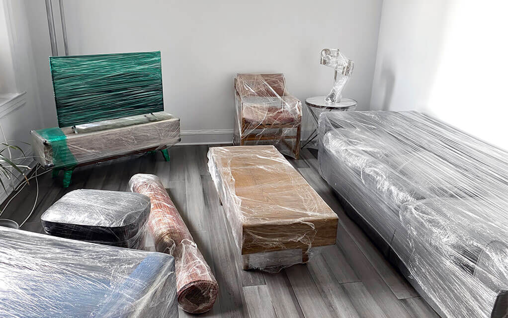 View of a living room with furniture, a rug, and a flat screen TV all wrapped securely in shrink wrap, waiting to be moved