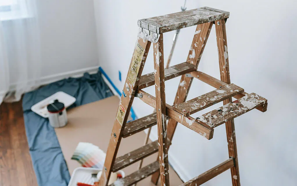 View of a ladder with pain stains all over it used for painting as a drop cloth with some carboard on it and paint swatches lay on the floor with it