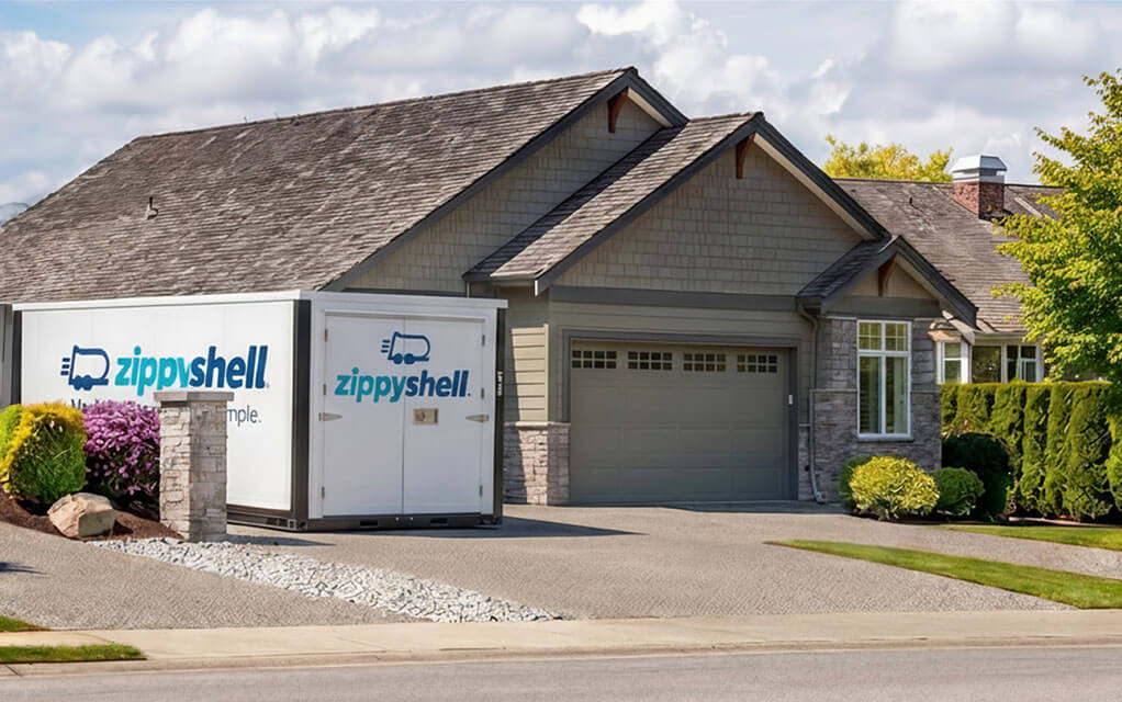 A Zippy Shell branded portable storage container sits in the driveway of a home in a suburban neighborhood on a partly cloudy day