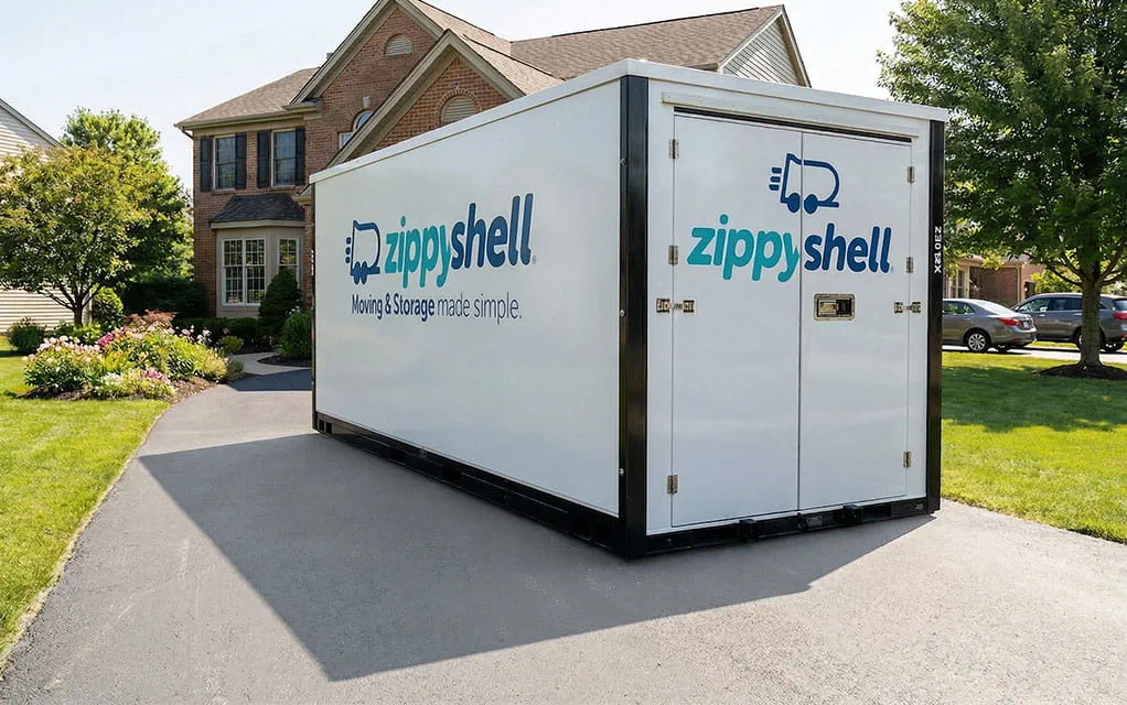 A Zippy Shell portable storage unit sits in the driveway of a large suburban home on a bright and sunny day