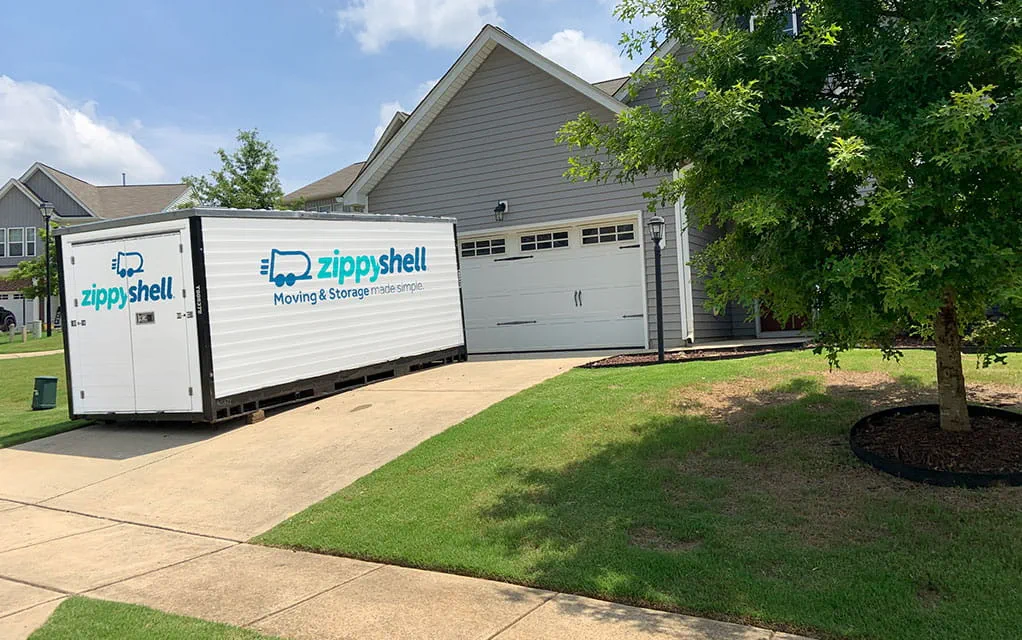 A Zippy Shell branded portable storage container sits in a home's driveway waiting to be packed for a move