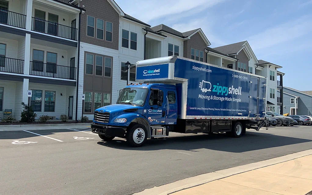 The front side view of a blue Zippy Shell branded moving truck waiting in the parking lot of an apartment complex