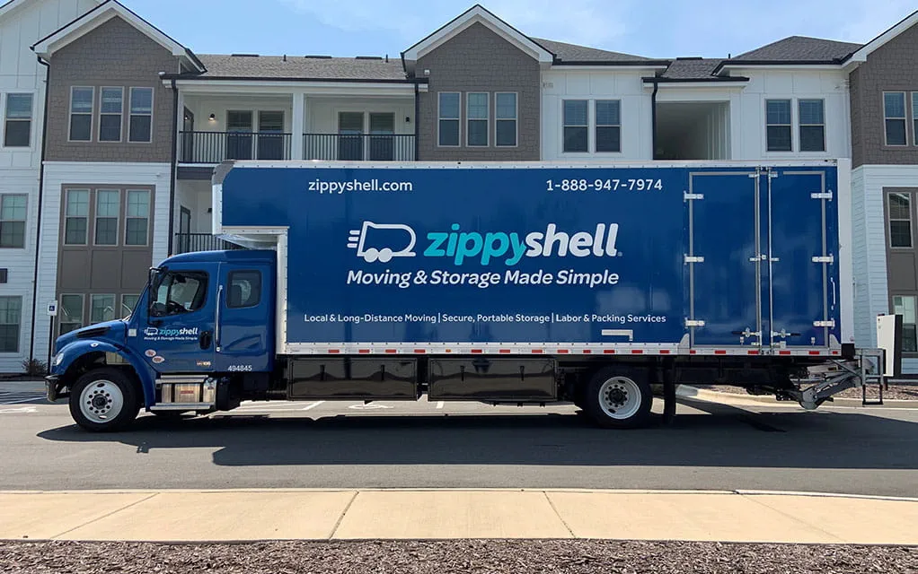 The side view of a blue Zippy Shell branded moving truck waiting in the parking lot of an apartment complex