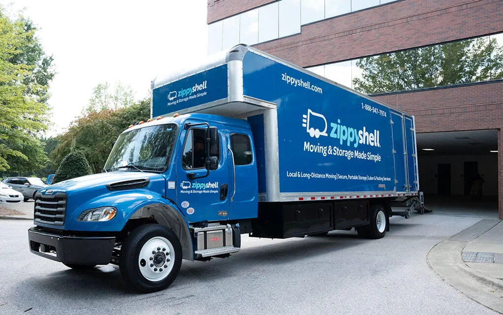 A Zippy Shell box truck in all blue sits parked outside of a commercial business location waiting to be packed