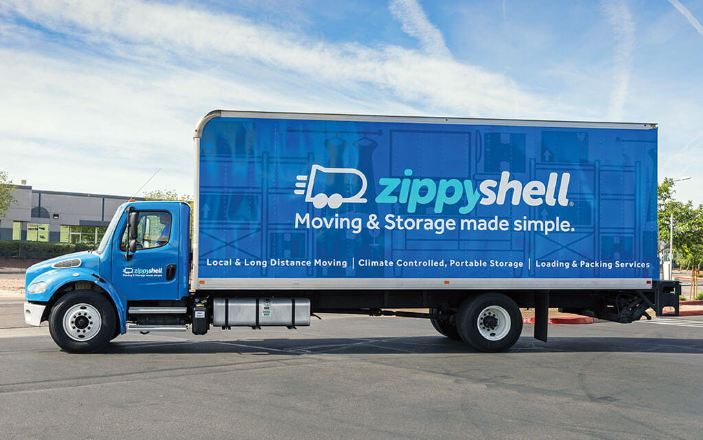 Side view of a large, blue Zippy Shell box truck waiting in a parking lot