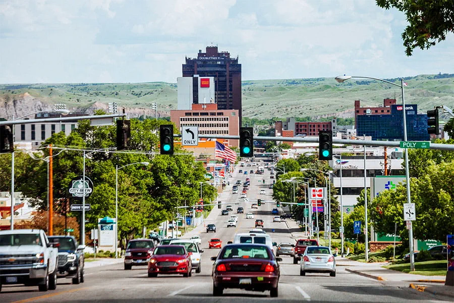 A view of downtown Billings, MT from afar down a busy downtown street lined with vehicles on a partly sunny day.