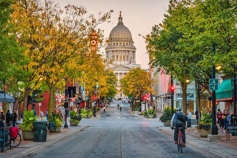 A view down a downtown street at sunset in downtown Madison, WI with the Wisconsin State Capitol Building in the background at the end of the street