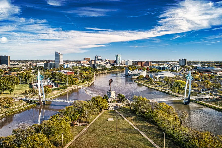 A view of The Keeper of the Plains monument at the fork of the Arkansas and Little Arkansas Rivers with the Wichita, Kansas downtown skyline in the background on a sunny day