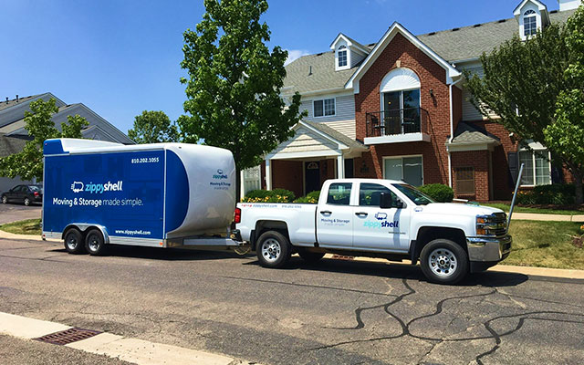 A Zippy Shell truck sits in front of a suburban home on the street with a Zippy Shell trailer attached to the back