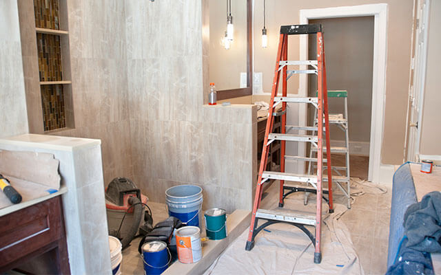A ladder, paint, and other renovation materials sit inside of a home's bathroom undergoing a renovation