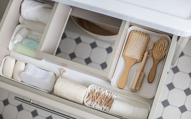 A drawer stands open with brushes, q tips, cotton swaps, and more all in containers in the bathroom's drawer