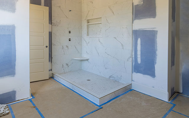 View of a bathroom undergoing a renovation, with a marble stone shower wall and floor surrounded by unpainted walls and floors awaiting floorboard or tile